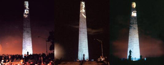 This image shows three side-by-side photographs of the Bunker Hill Monument at night with images of people’s faces projected on its surface. Crowds and a statue can be seen in front of the monument.