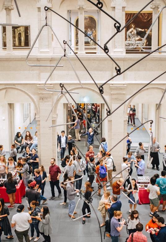 A courtyard full of people chatting, with paintings on display in the upper level.