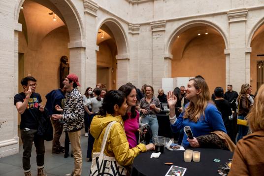 A courtyard filled with visitors chatting over drinks at high top tables.