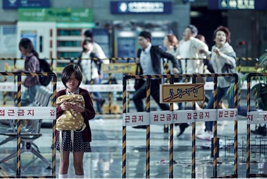 A little girl stands amid a chaotic scene behind her.