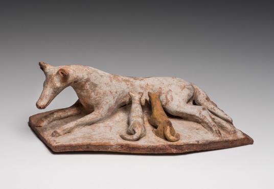 Terracotta figurine depicting a dog nursing two puppies on her left side.