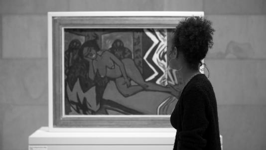 A black and white image of a woman looking at a painting of a nude female figure.