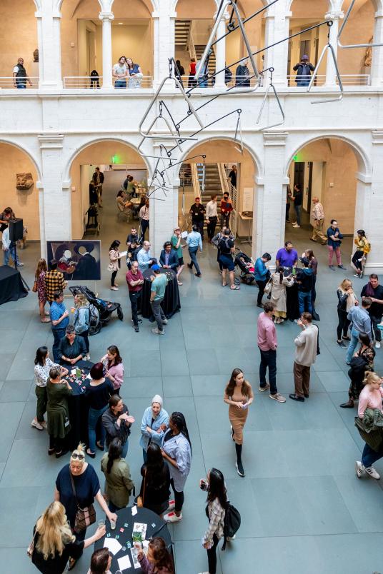 A courtyard full of people chatting, with paintings on display in the upper level.