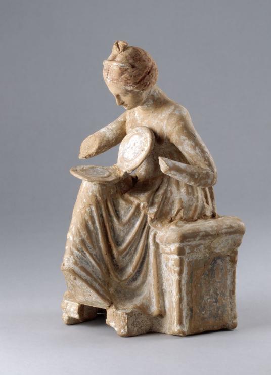 A terracotta figurine depicting a seated young woman with a mirror on her lap.