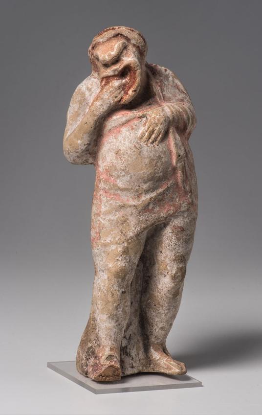 Terracotta figurine of a figure wearing a short tunic and a full-face mask with a wide, open mouth.