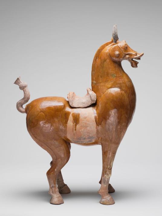 Side view of a sculpture of a brown horse wearing a beige blanket and saddle.