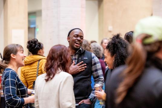 A group of people stand in the middle of a crowd smiling and laughing.