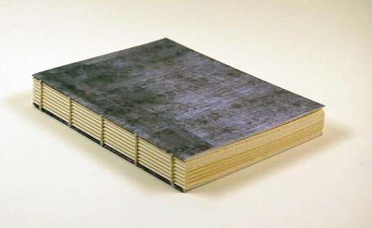 A small bluish-gray book with an exposed sewed binding sits at an angle on a white surface.