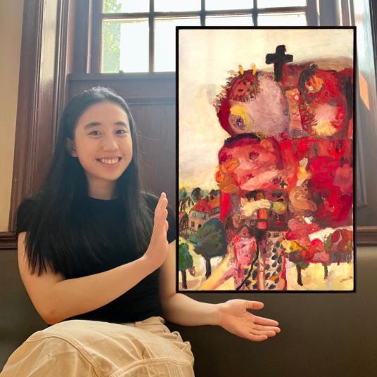 In this photomontage, a smiling young woman gestures toward a painting that appears to be floating. She sits on a bench below a window. The painting incorporates broad strokes of mostly red and yellow and shows a heap of ragged bodies, topped by a cross, that nearly crowds out a view of houses and trees.