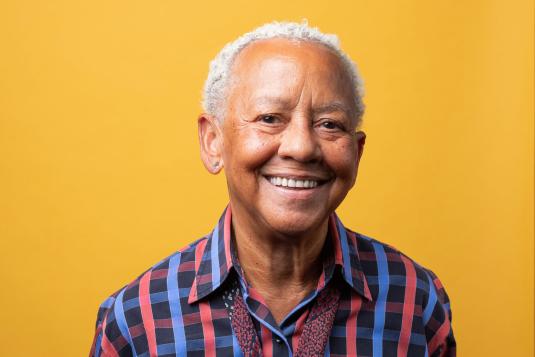 A colorful photograph shows an older Black woman with short and curly white hair smiling at the viewer.