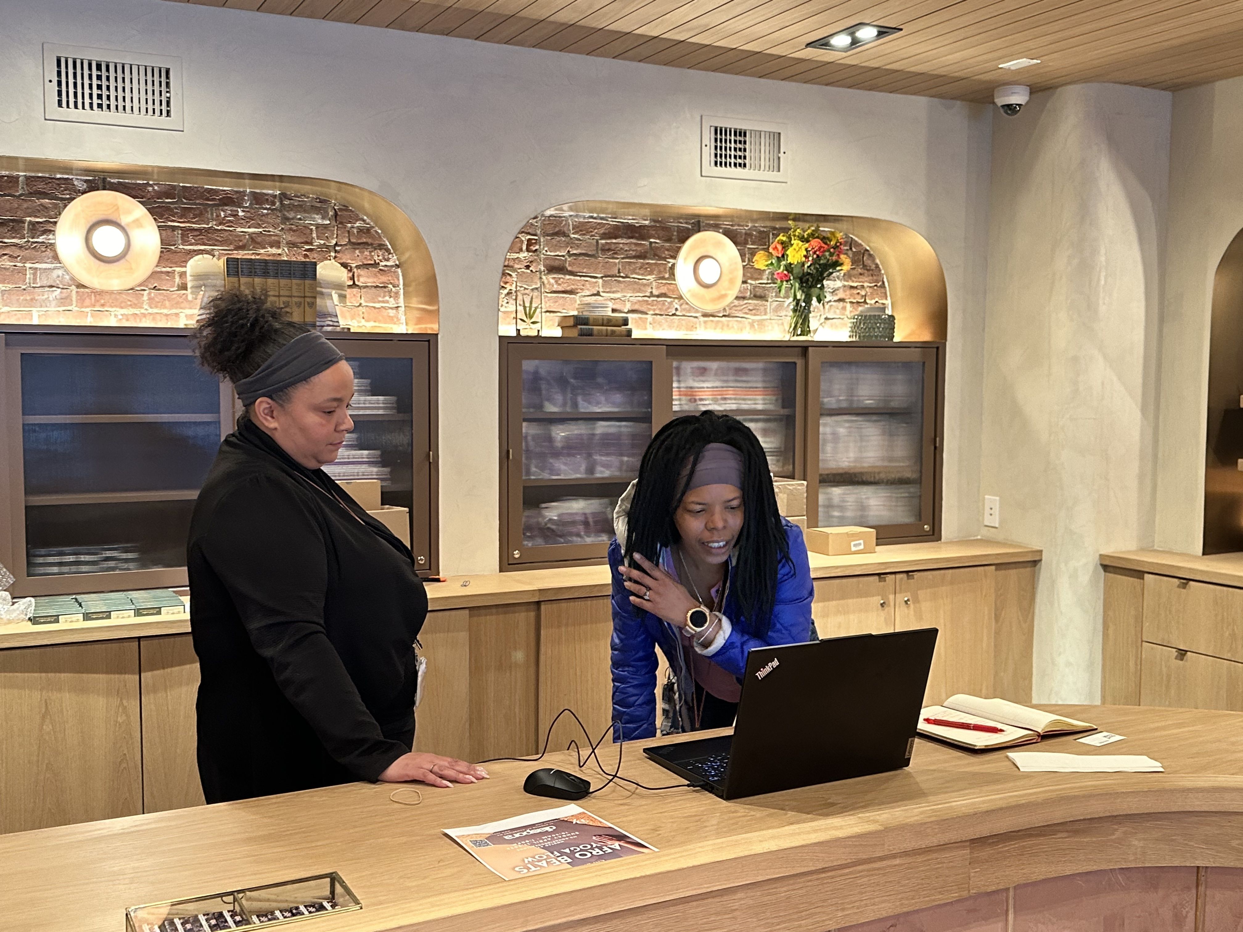 Yamba Boutique GM Shani Joseph, left, looks on as CEO Leah Samura, right, bends over to look at a laptop screen inside Yamba Boutique.