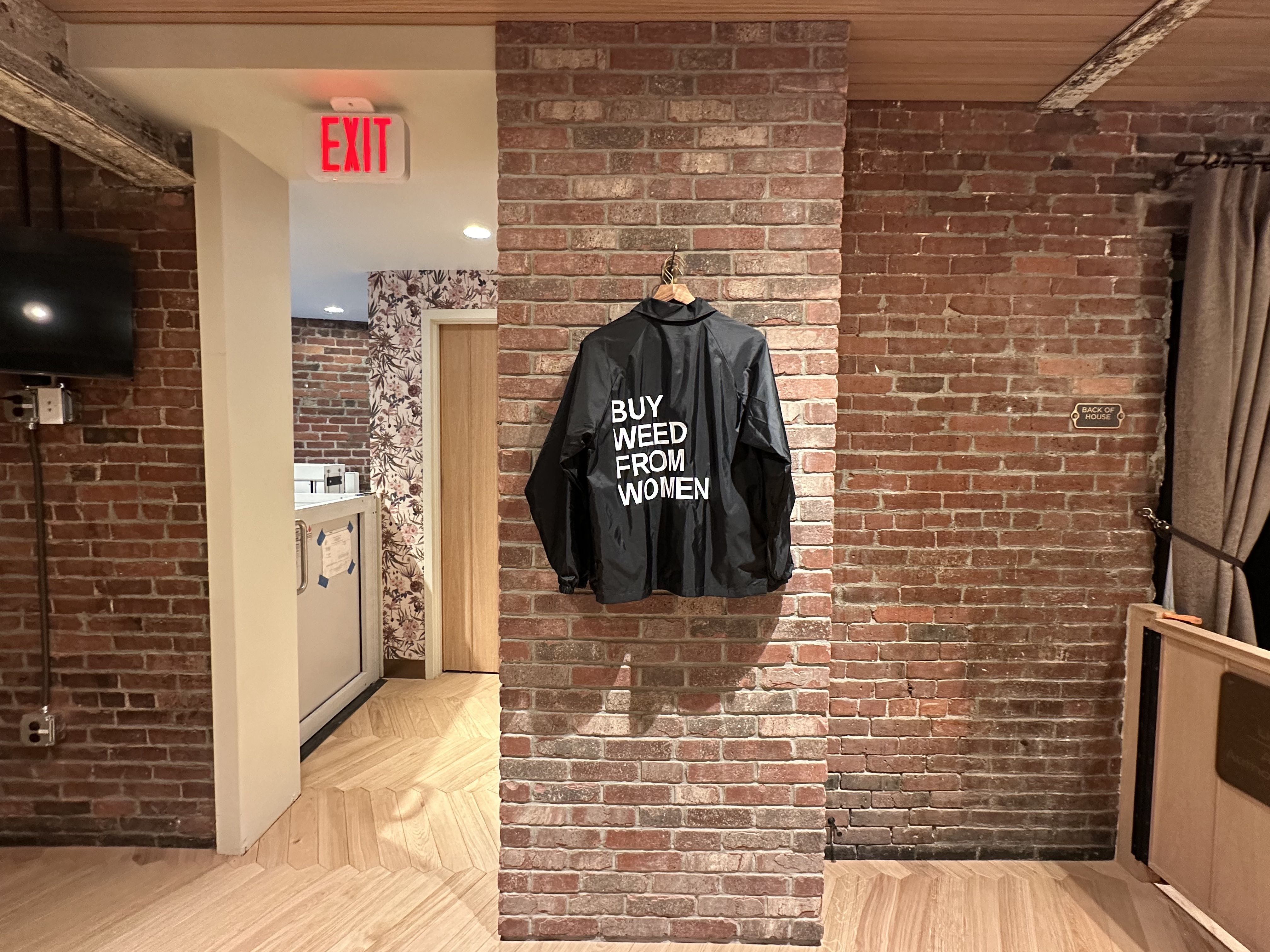 A black jacket that states "Buy Weed From Women" hands on the wall at Yamba Boutique, one of several pieces of apparel for sale at the dispensary. 