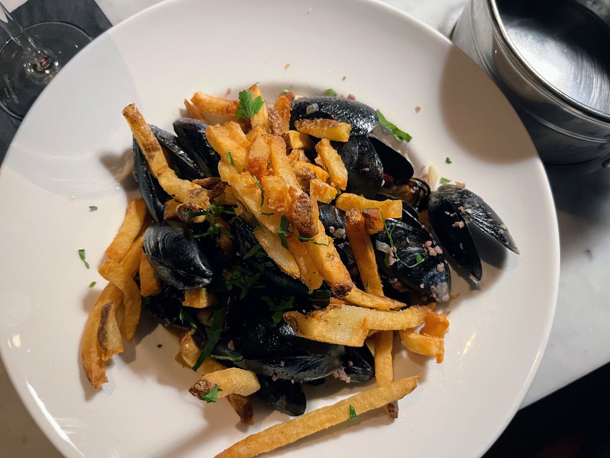 A white plate filled with black-shelled mussels mixed with fries.