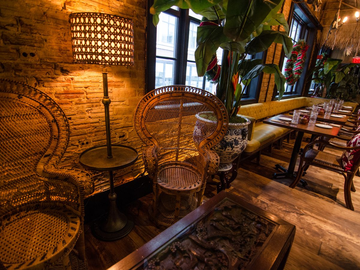 Two wooden peacock-style chairs sit in front of an intricately carved wooden table in a tiki-themed restaurant.