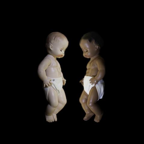 two baby dolls face each other, one white and one black.